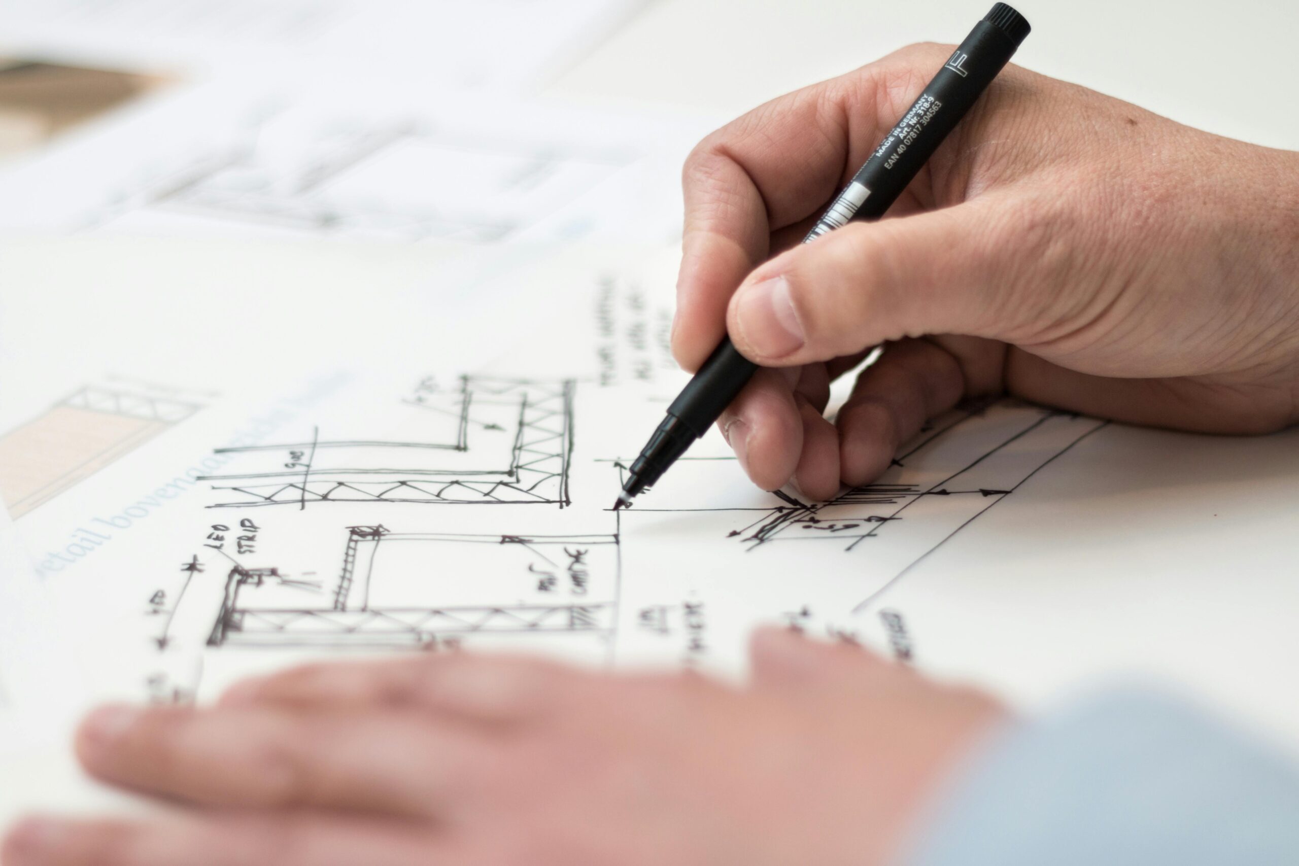 Home Close-up of hand drawing intricate technical designs on blueprint with pen, ideal for engineering or architecture themes.
